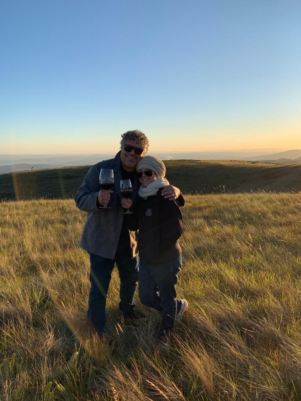 Bilu Carlinho e a esposa brindando com vinho no pôr do sol da serra