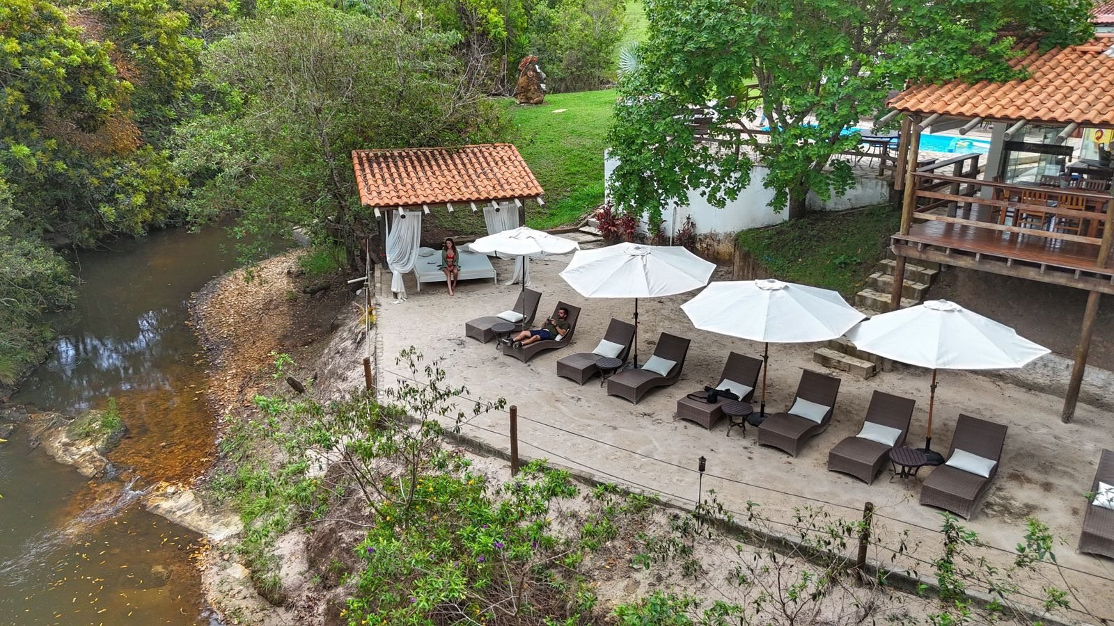Vista do alto do riacho e da prainha natural, com espreguiçadeiras e ombrelones